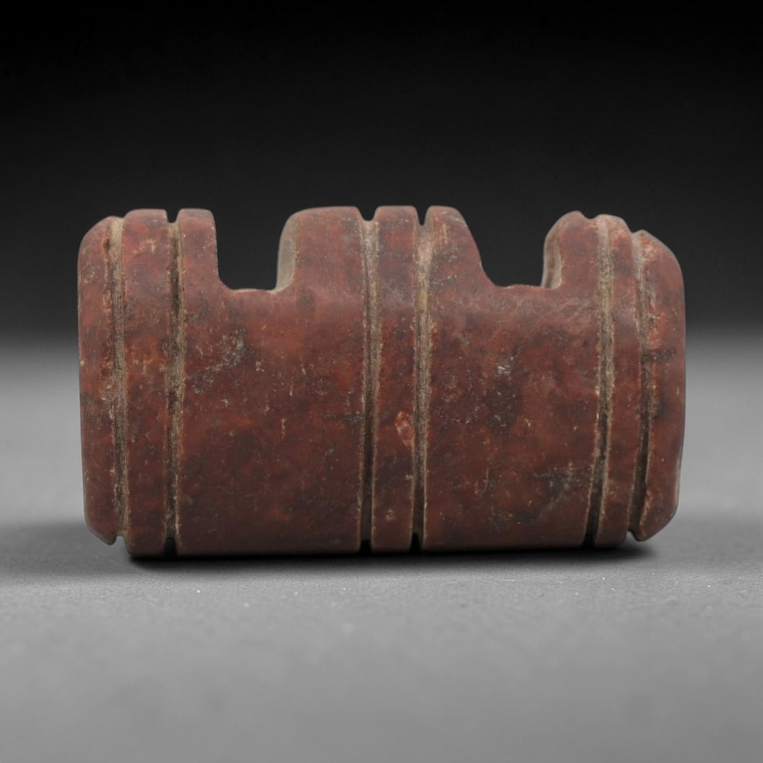 Ancient Near Eastern Red Stone Double Amulet - Carved Bead, 29ZV: This amulet is carved from a rich, reddish-brown stone with subtle lighter veining, likely brecciated jasper or red steatite. It features a distinctive symmetrical double-form design with three horizo