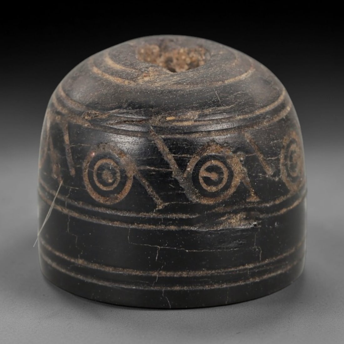 Ancient Bone Spindle Whorl - Near Eastern Curvilinear Motif, 89XR: This ancient Near Eastern spindle whorl is crafted from bone, featuring incised curvilinear and dot patterns encircling the central perforation. The compact, rounded form is a traditional textile tool