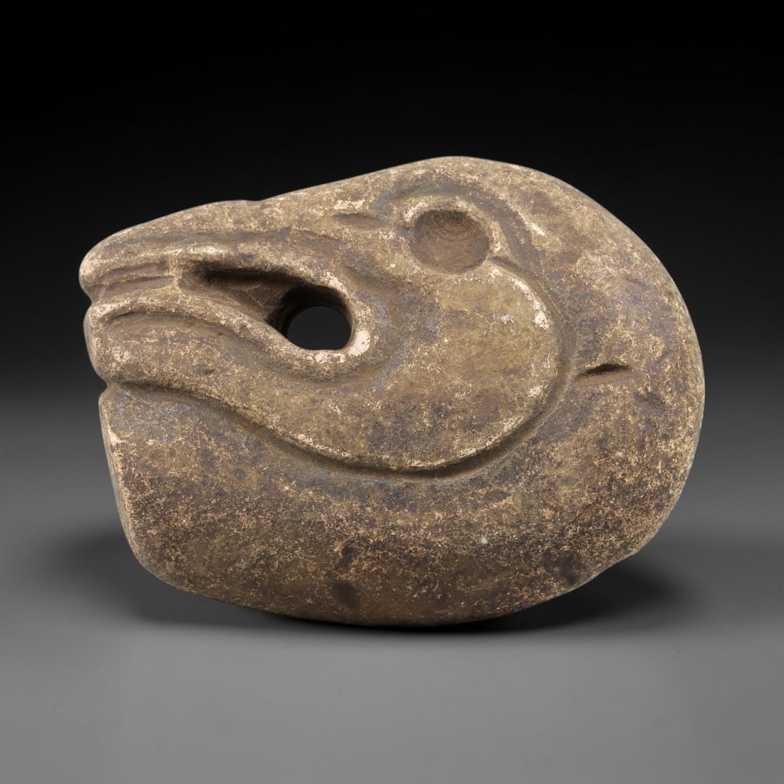 Ancient Stone Zoomorphic Head Amulet - Near Eastern Figurine, 95FX: Carved from a dense, granular stone, this amulet depicts a stylized zoomorphic head-likely a canine or equine-in profile, with incised relief details defining the snout, circular eye socket, and a per