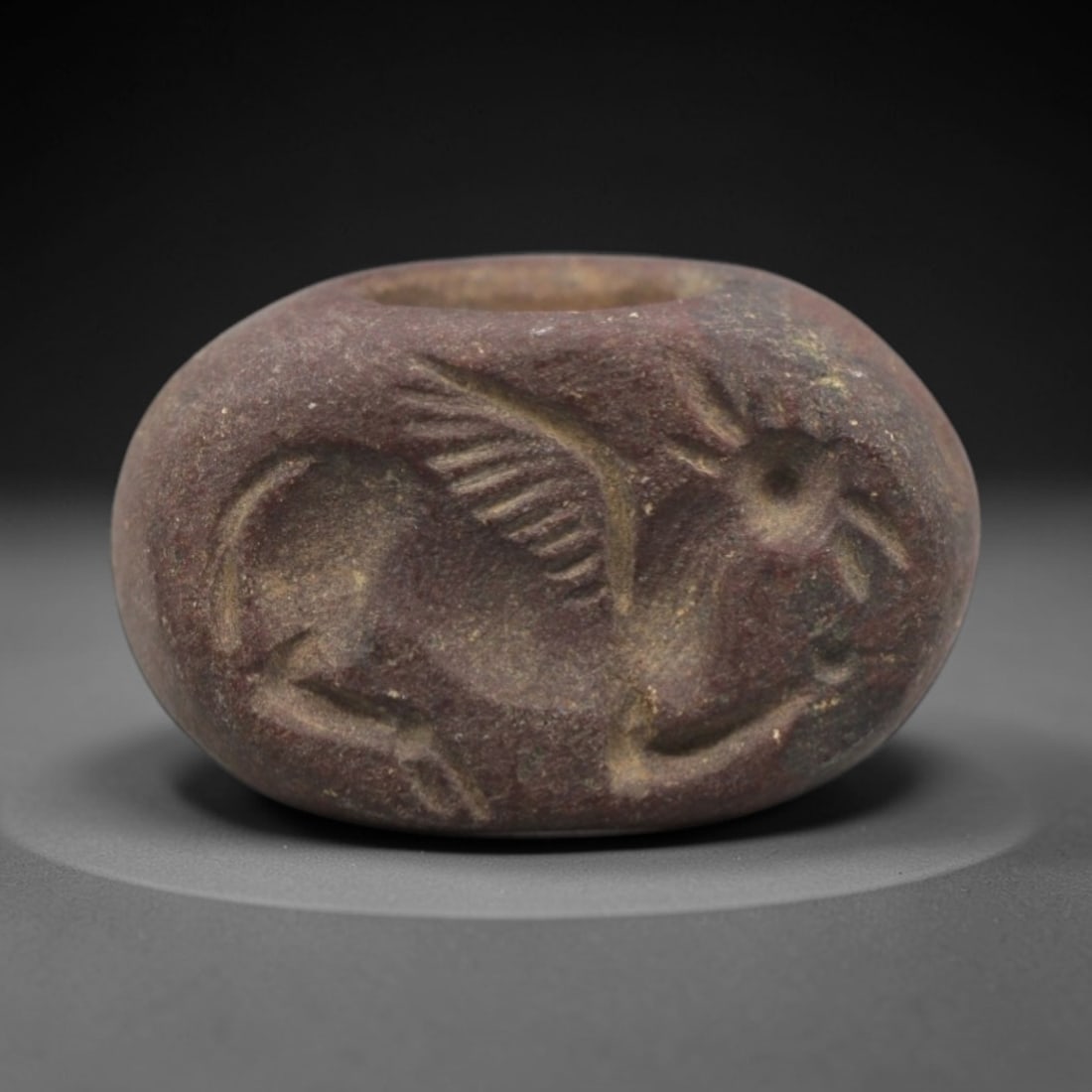 Ancient Stone Hemispherical Stamp Seal - Near Eastern Winged Bull Amulet, 1ZS: This ancient Near Eastern hemispherical stamp seal is carved from a dense, reddish-brown stone, likely steatite or chlorite, with a weathered, earthy patina and natural surface pitting. The seal's ova