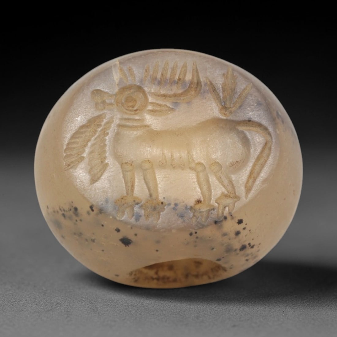 Ancient Chalcedony Hemispherical Stamp Seal - Near Eastern Bull Figure, 34ZP: Crafted from translucent, speckled chalcedony, this hemispherical stamp seal bears a deeply incised depiction of a stylized bull, rendered in linear relief with distinct horned head, patterned torso,