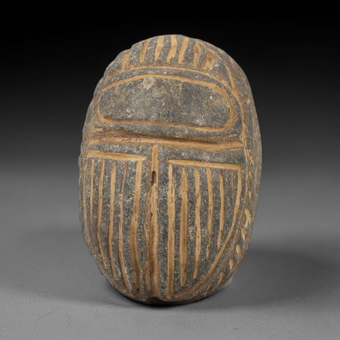 Ancient Egyptian Grey Stone Scarab - Amulet Figurine, 32AM: This artifact is a carved grey stone scarab amulet, crafted from a granular, dark grey stone with a textured surface and earthy patina filling the incised decorative details. The dorsal side features
