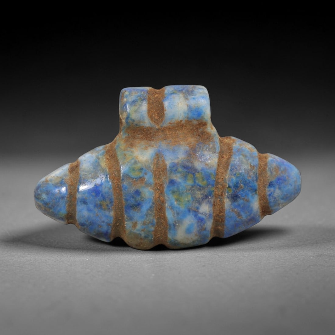 Ancient Lapis Lazuli Shell Form Amulet - Egyptian Ritual Pendant, 23ZT: Carved from lapis lazuli, this amulet features a symmetrical double-pointed shell-like form with a raised upper lug pierced for suspension, its body incised with vertical bands that define its segment
