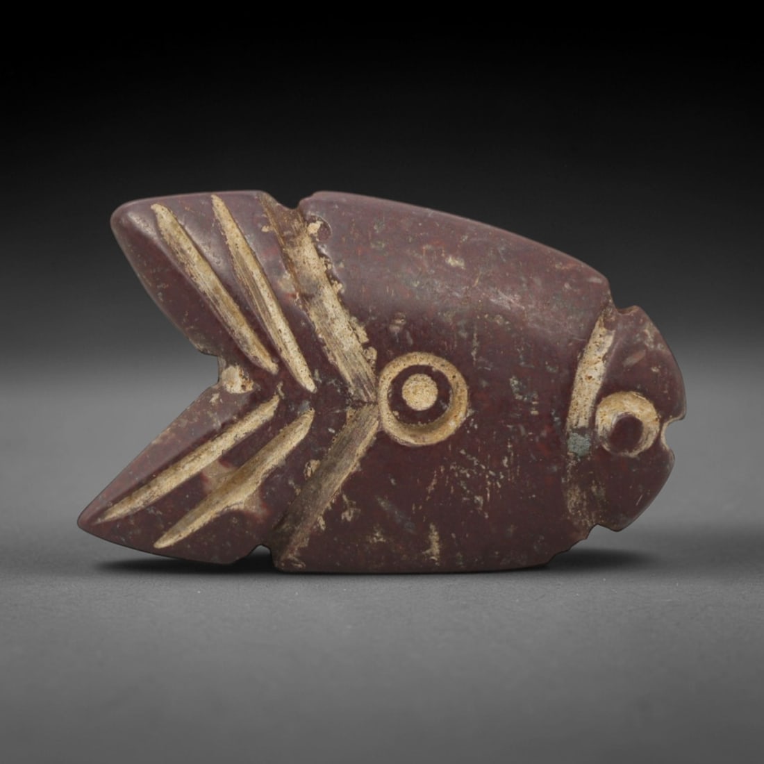 Ancient Stone Fish Amulet - Egyptian Animal Pendant, 35XQ: This amulet is carved from a rich, deep red stone, shaped into a stylized fish form with incised linear details defining the fins, eye, and facial features. The body is flat and streamlined, with a di