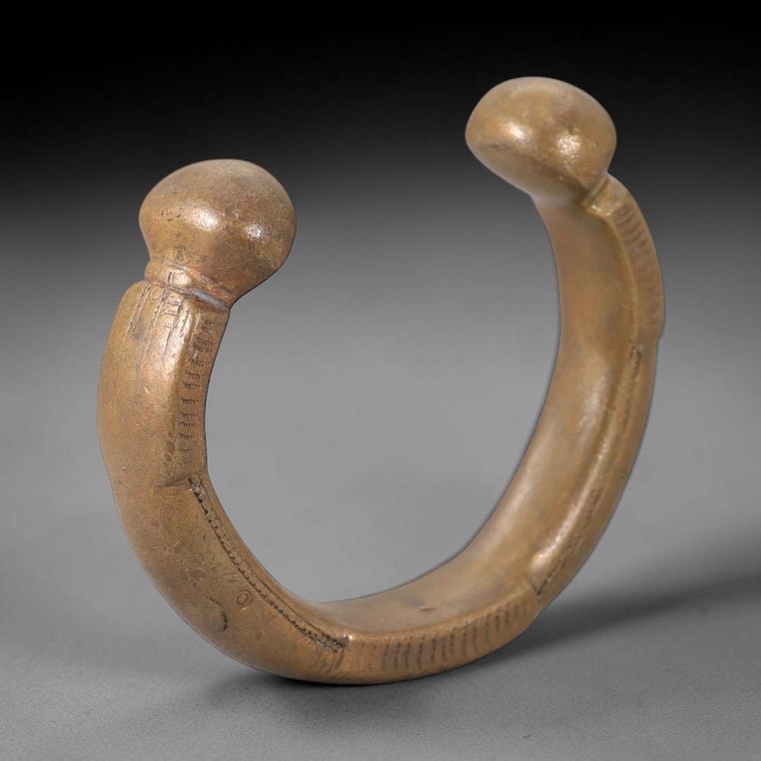 African Bronze Queen Manilla - West African Bracelet Currency, 96FW: Cast from warm golden-brown bronze, this 6.5cm diameter queen manilla features a robust C-shaped form with two bulbous terminal ends, adorned with intricate incised linear and geometric detailing alon