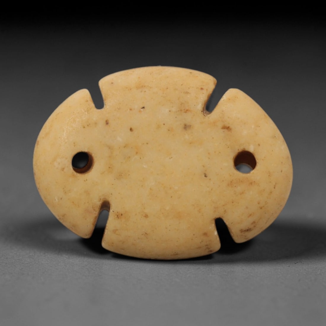 Ancient Stone Cosmic Amulet - Near Eastern Pendant, 8XR: Carved from pale beige stone, this amulet features an oval body with symmetric notches along the edge and two lateral suspension holes. The geometric, abstract design is characteristic of Ancient Near
