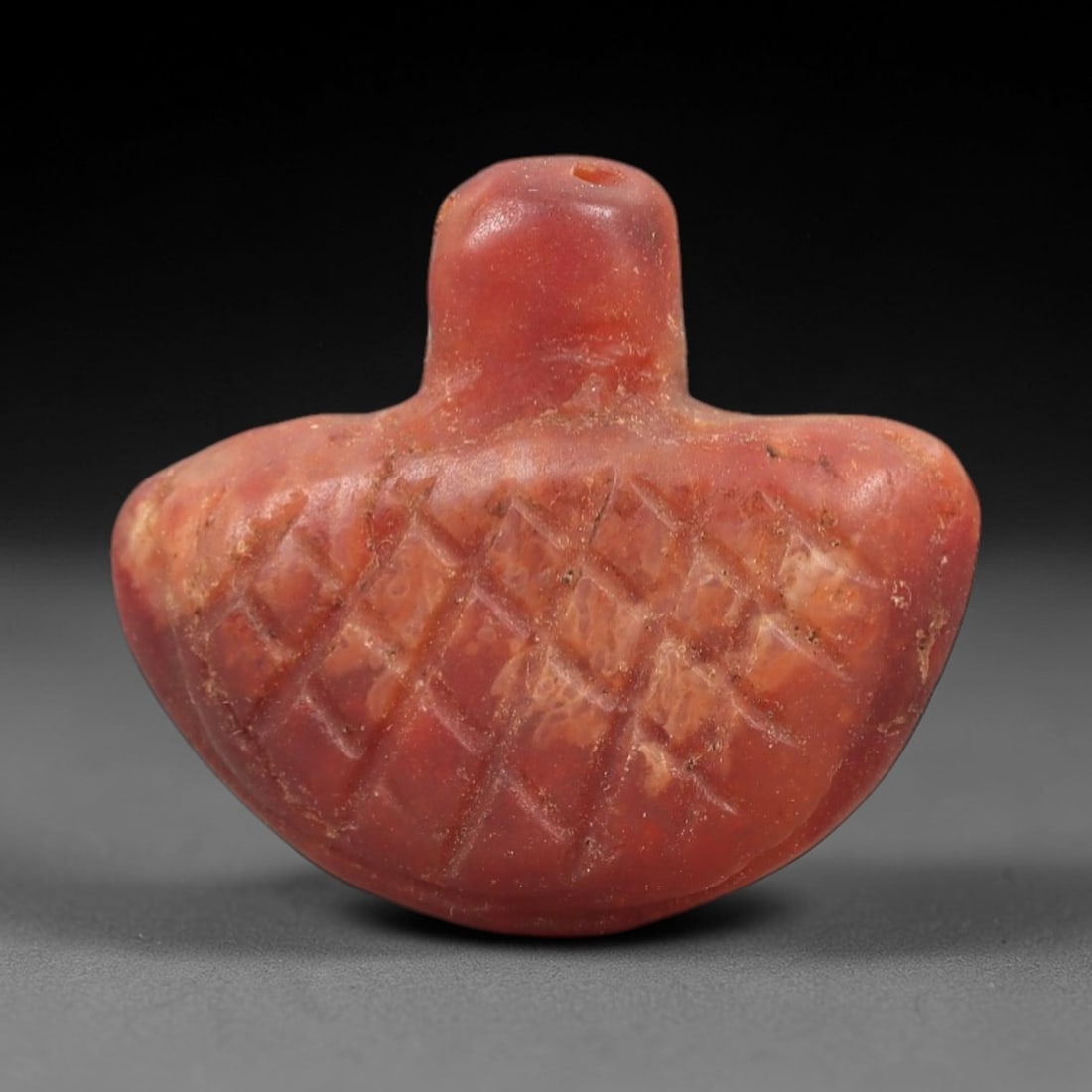 Ancient Carnelian Bird Amulet - Egyptian Figurine, 42XS: This amulet is carved from warm, reddish-orange carnelian, featuring a compact, stylized avian form with a pierced suspension hole at the dorsal apex, confirming its function as a wearable protective