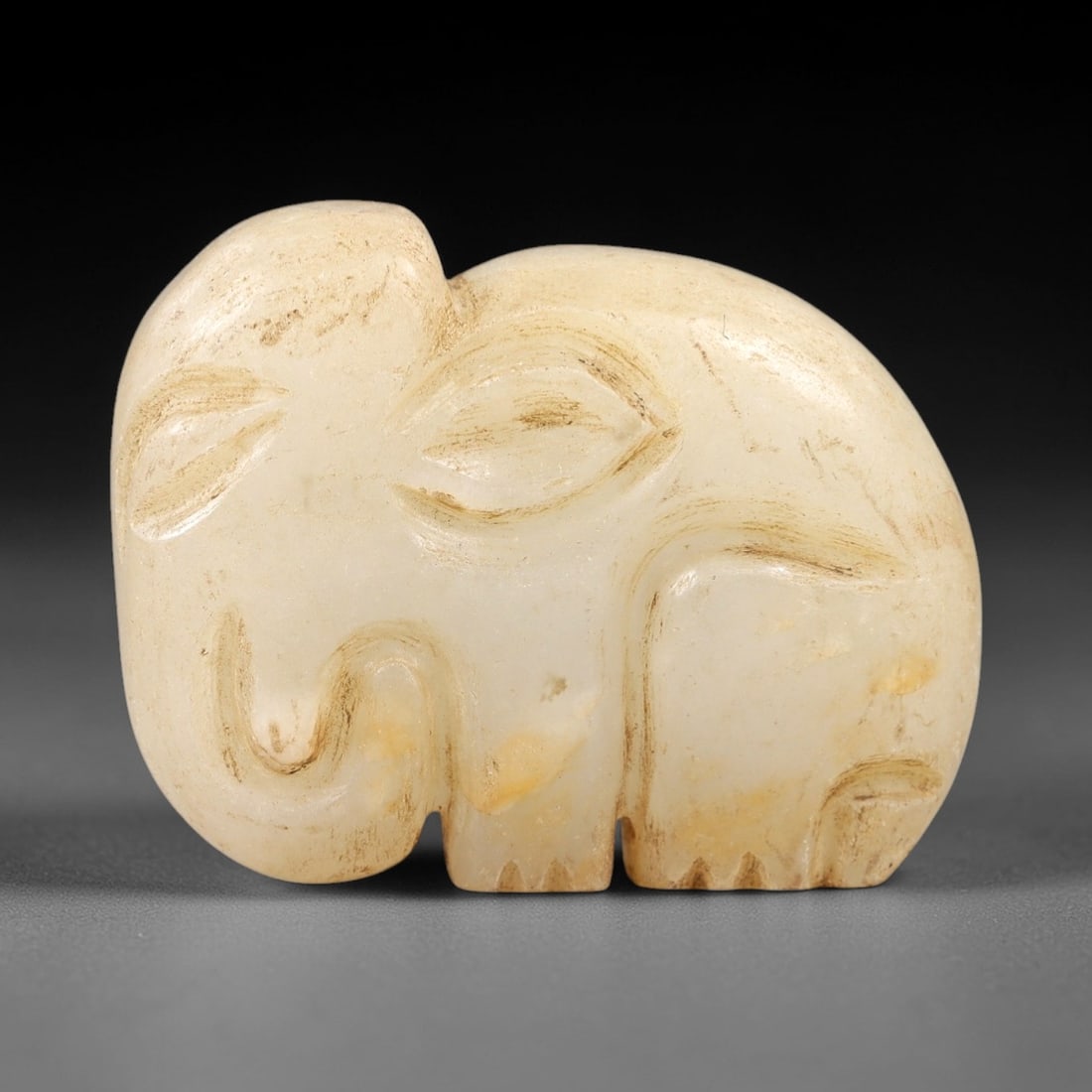 Ancient Chalcedony Elephant Amulet - Near Eastern Animal Pendant, 25AK: Carved from pale milky chalcedony, this stylized elephant amulet features a compact rounded form with simplified incised details defining its ears, curled trunk, and stubby legs. The smooth polished s