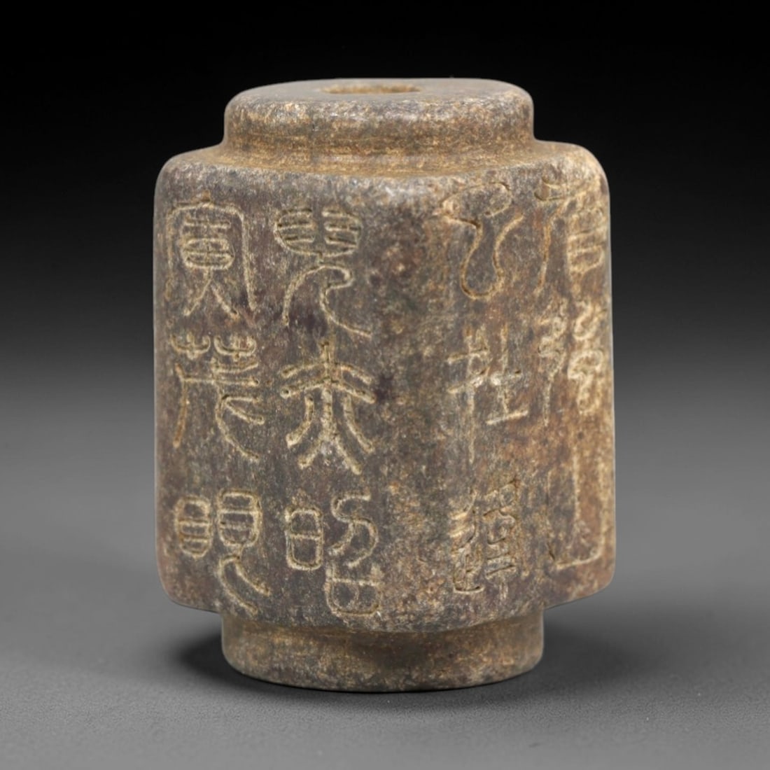 Antique Chinese Inscribed Bead - Seal Script Pendant, 56ZP: This cylindrical antique bead is carved from a mottled, earthy-toned stone, featuring a central perforation for stringing, with vertical incised seal script inscriptions wrapping around its faceted si