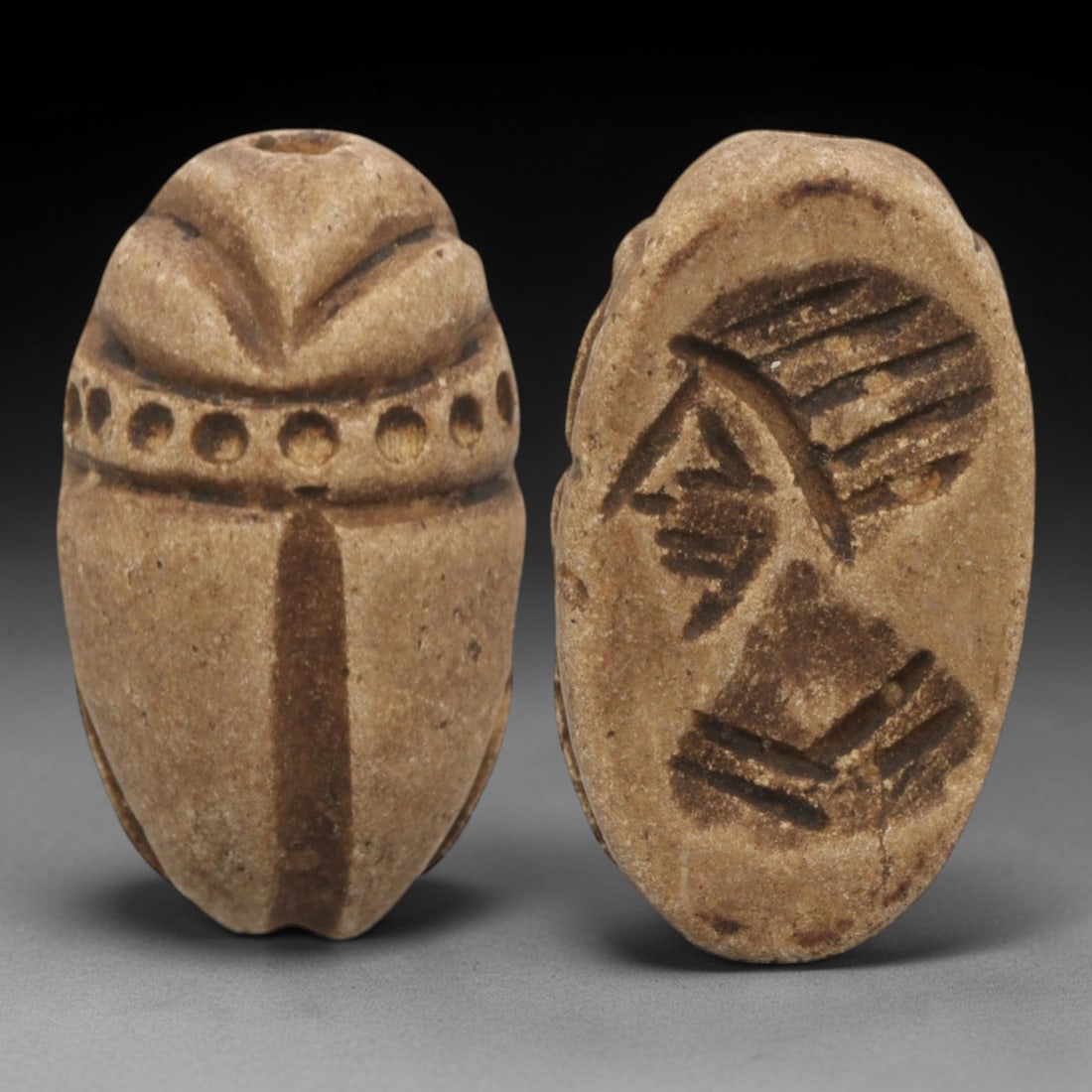 Ancient Near Eastern Scarab Stamp Seal - Anthropomorphic Profile Intaglio, 3ZS: Carved from a light tan, porous stone, this oval scarab stamp seal features a classic scaraboid dorsal form, with incised linear patterns defining the beetle's elytra and a row of eight circular decor
