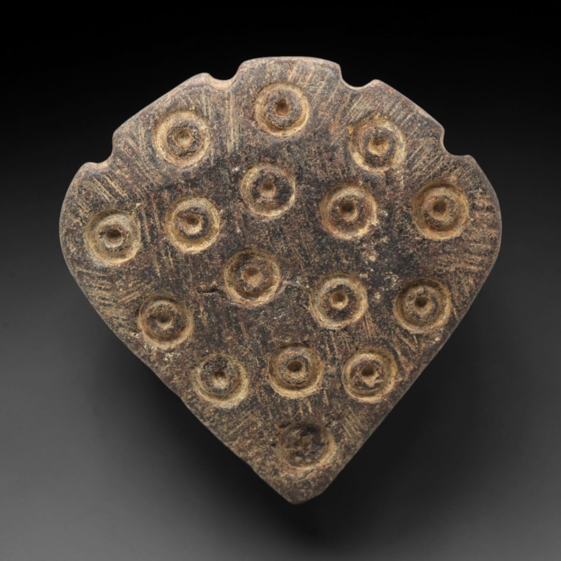 Ancient Steatite Amulet - Near Eastern Concentric Circles, 52XV: Carved from steatite, this ancient amulet displays a shield-shaped form adorned with thirteen raised concentric circle motifs, each centered with a dot, executed in raised relief typical of Near Easte