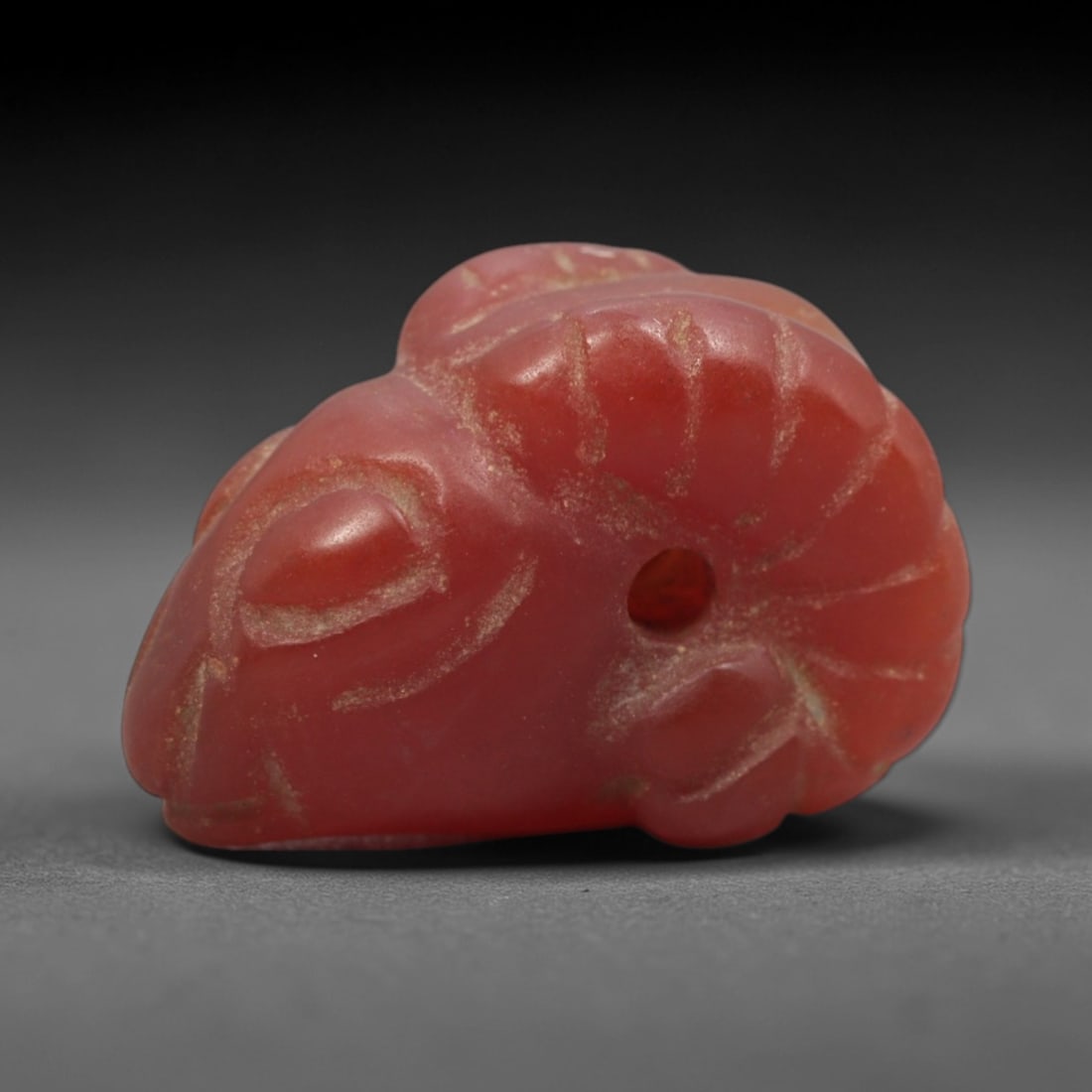 Ancient Carnelian Ram Head - Near Eastern Amulet Figurine, 70XS: Carved from rich, opaque carnelian with natural surface patination and wear, this amulet depicts a stylized ram's head, defined by prominent curved horns, simplified facial contours, and incised linea