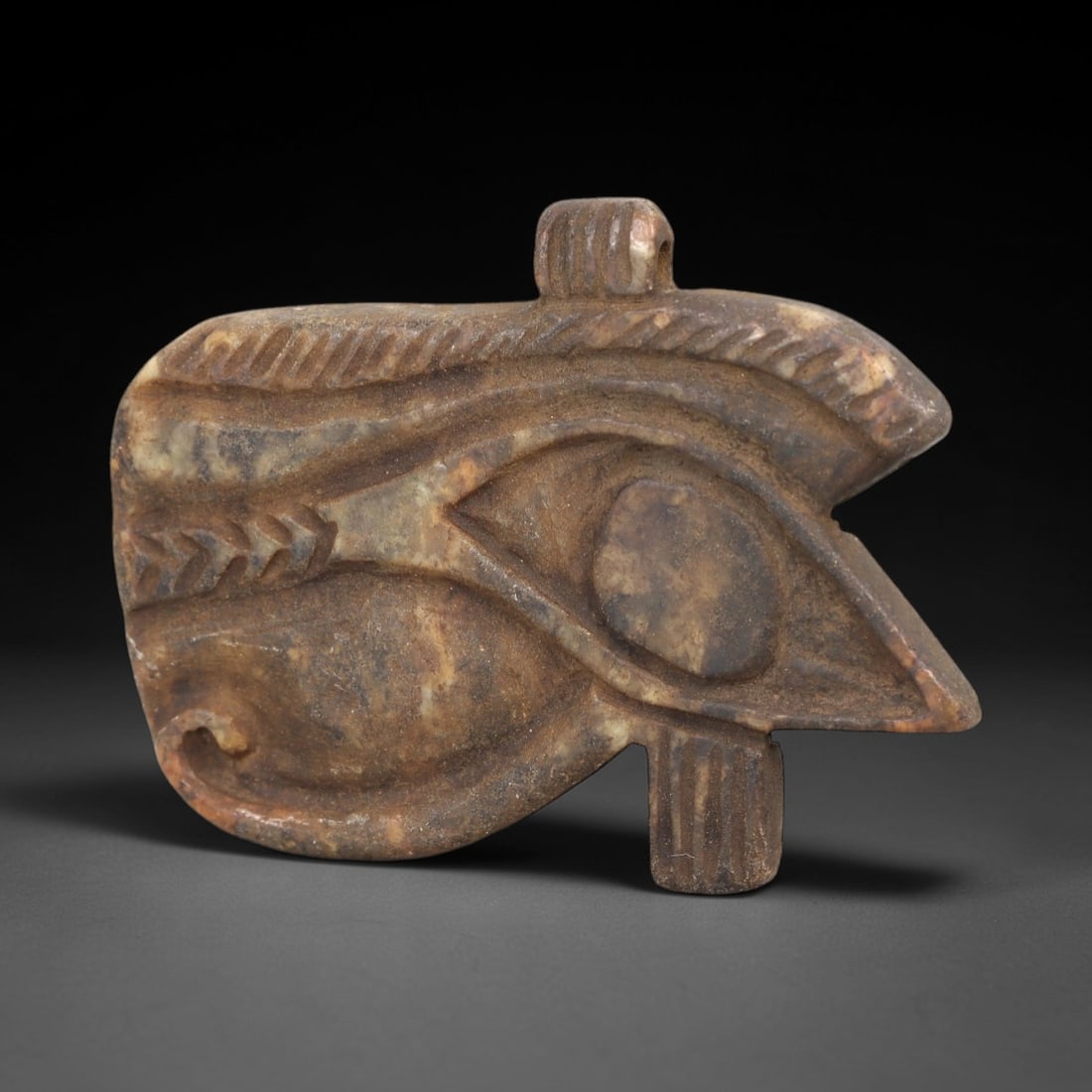 Ancient Stone Wedjad Eye - Egyptian Amulet Figurine, 20AM: Carved from a mottled, earth-toned stone, this Wedjad Eye amulet adheres to the canonical Egyptian iconography of the Eye of Horus, with distinct incised details defining the brow, pupil, and facial c