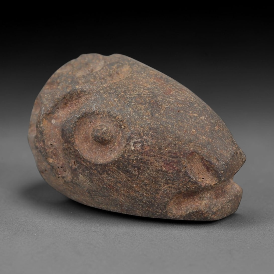 Ancient Hematite Ram Head Bead - Near Eastern Amulet, 16AH: Carved from hematite, this ancient Near Eastern ram head bead features a stylized facial rendering with distinct eye and horn details, crafted in the primitive yet expressive style typical of regional