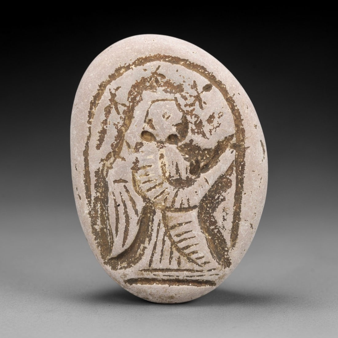 Ancient Stone Angel Amulet - Near Eastern Christian Figurine, 66ZV: Carved from a smooth oval stone, this piece features a bas-relief depiction of an angel in a praying pose, with incised lines defining the wings, flowing robes, and halo adorned with cross motifs, con