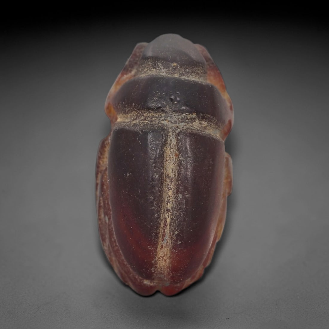 Ancient Carnelian Scarab Amulet - Egyptian Figurine, 39AJ: Carved from rich, deep red carnelian with natural amber-orange gradients, this amulet is formed as a stylized scarab beetle with incised linear detailing to define segmented head plates, central body