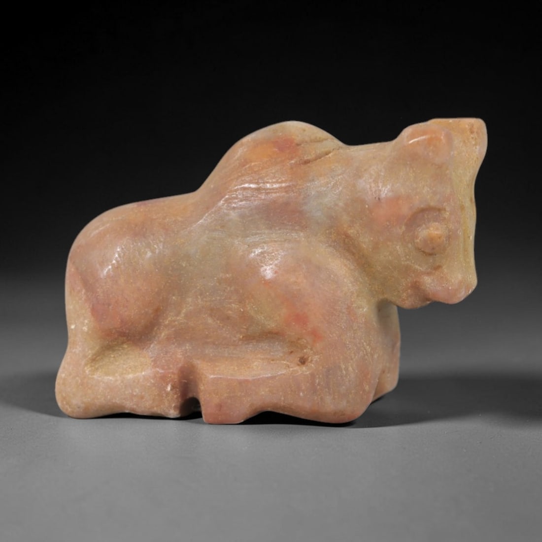 Ancient Stone Bovine - Near Eastern Animal Figurine, 99AP: This artifact is carved from a warm, variegated stone with subtle pink and beige tonal variations, exhibiting a smooth, polished surface with faint mineral striations. The form is a stylized bovine, l
