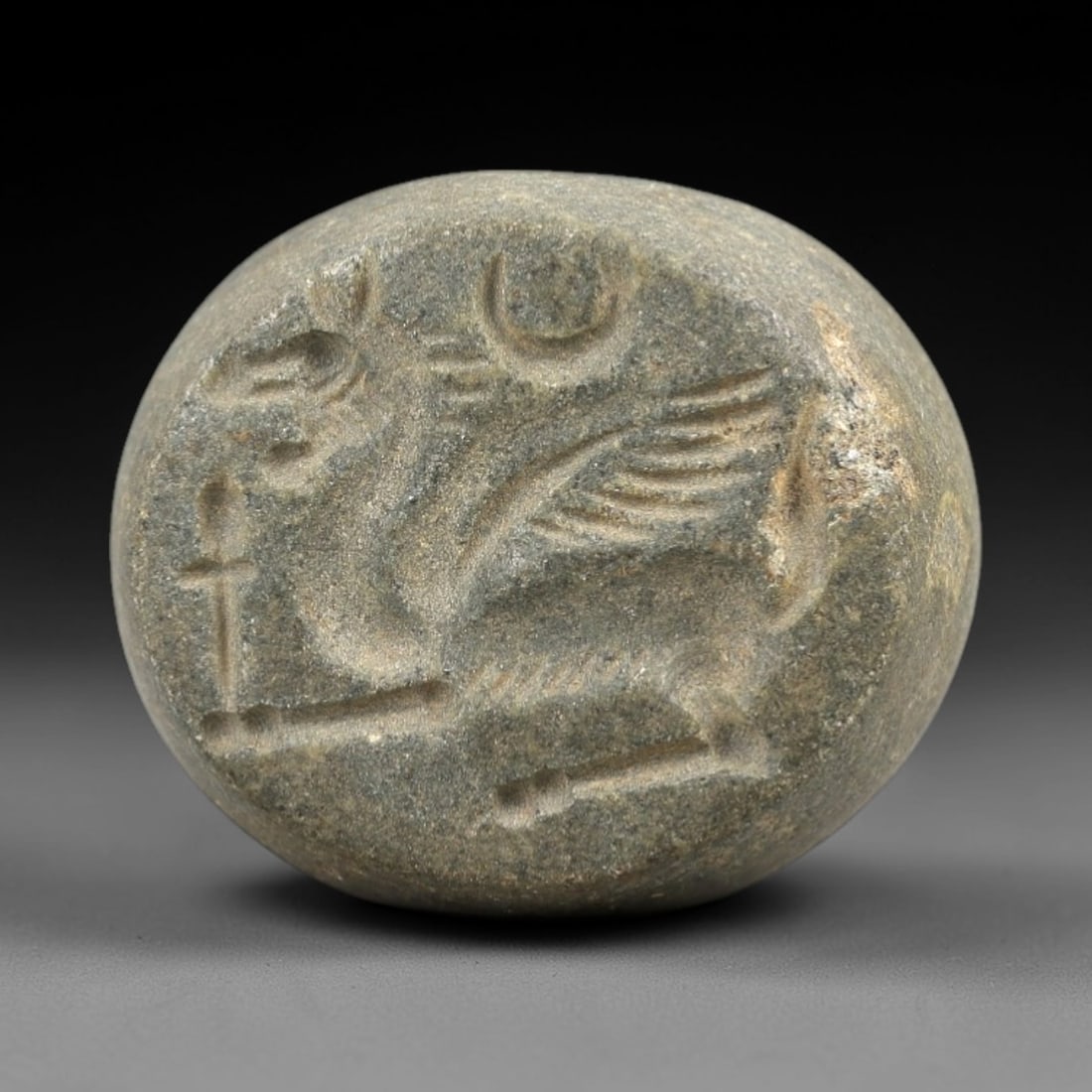 Ancient Stone Hemispherical Stamp Seal - Near Eastern Winged Bull Amulet, 9AN: This ancient Near Eastern hemispherical stamp seal is carved from a dense, weathered stone, likely chlorite or steatite, exhibiting a muted, earthy patina from millennia of burial. The seal's circular