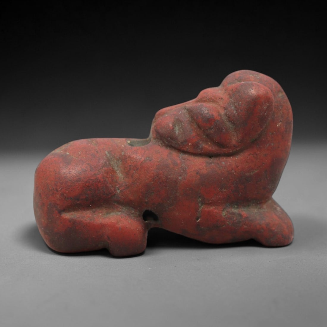 Ancient Near Eastern Red Stone Ram Amulet - Carved Figurine, 21ZV: This amulet is carved from a rich, reddish-brown stone, likely brecciated jasper or red steatite, with subtle incised details defining its recumbent ram form. The piece depicts a ram in a resting pose