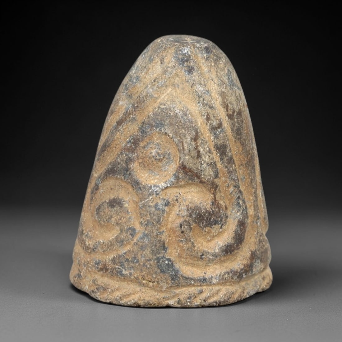 Ancient Stone Ritual Relic - Gandharan or Central Asian Stylized Motif, 63AM: This conical stone relic is carved from a dense, micaceous stone with a heavily weathered, multi-toned patina ranging from sandy beige to deep charcoal streaks. The form tapers from a rounded base to