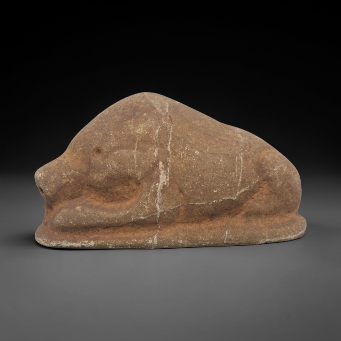Ancient Stone Boar - Near Eastern Animal Figurine, 42FX: Carved from a coarse, earthy stone, this recumbent boar figure exhibits simplified, rounded forms with incised lines defining the limbs, facial contours, and snout. The compact, robust posture and sty