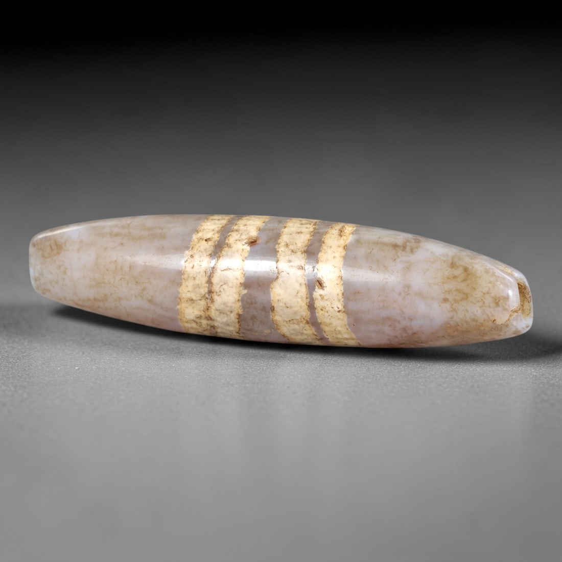 Ancient Agate Striped Dzi Bead - Himalayan Amulet, 13AS: Crafted from translucent agate, this elongated bead displays four parallel etched horizontal bands, executed in the traditional Himalayan Dzi bead technique. The form is tapered and cylindrical, with