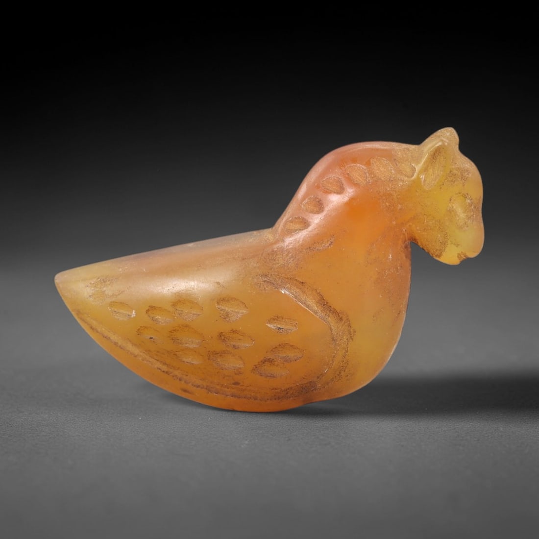 Ancient Agate Bird Amulet - Near Eastern Animal Pendant, 70AK: Carved from translucent golden-orange agate, this stylized bird amulet features a compact avian form with a pointed beak, simplified facial features, and dotted incised patterns defining its wing feat