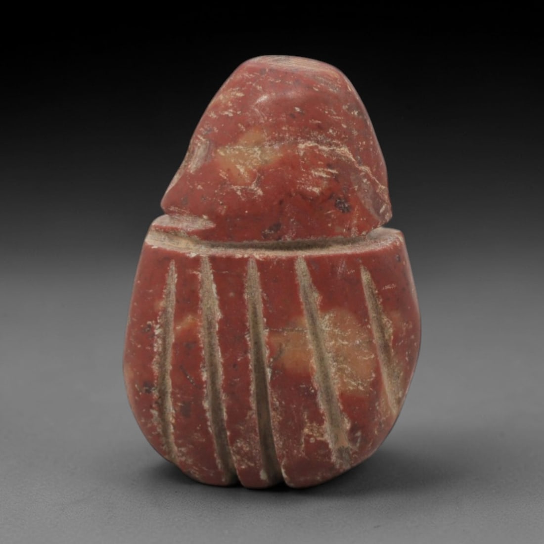 Ancient Stone Scarab - Egyptian Amulet Figurine, 51XR: Carved from reddish-brown stone, this amulet takes the form of a scarab beetle, with a domed head and a body incised with vertical linear details representing elytra. The iconography is characteristic