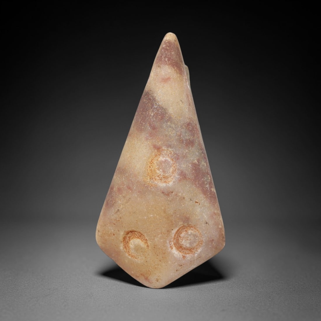 Ancient Beige Stone Amulet - Egyptian Style Figurine, 97AE: Carved from beige stone, this ancient Egyptian-style amulet features a compact, pointed form with three circular motifs on one side and a suspension hole at the top, indicating its use as a wearable a