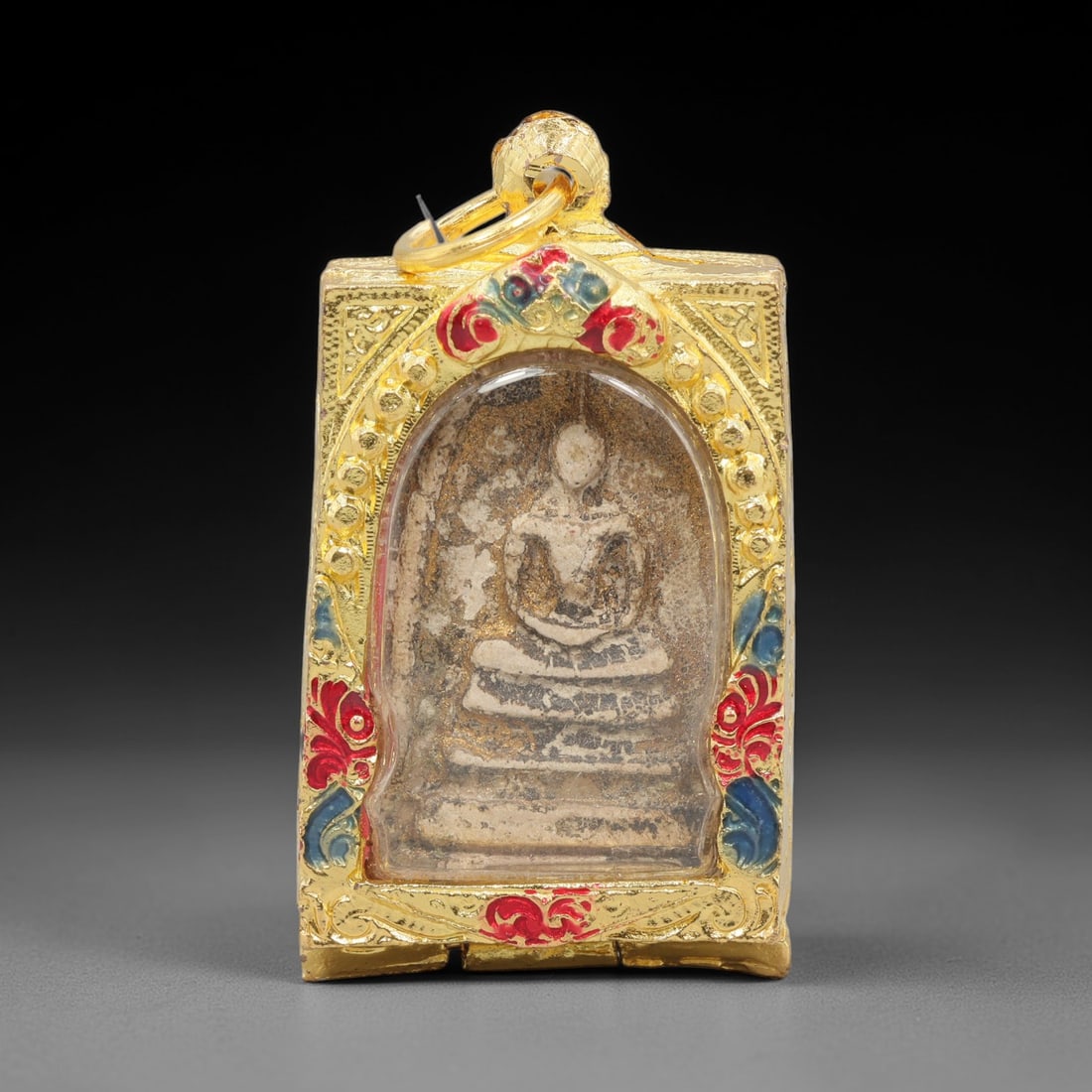 A Thai Terracotta Buddha Amulet in Metal Case, 20th Century, 71ZH: The amulet is formed from terracotta, with a light beige matrix containing visible particulate inclusions and surface discoloration. The obverse depicts a seated Buddha in meditative posture, seated o