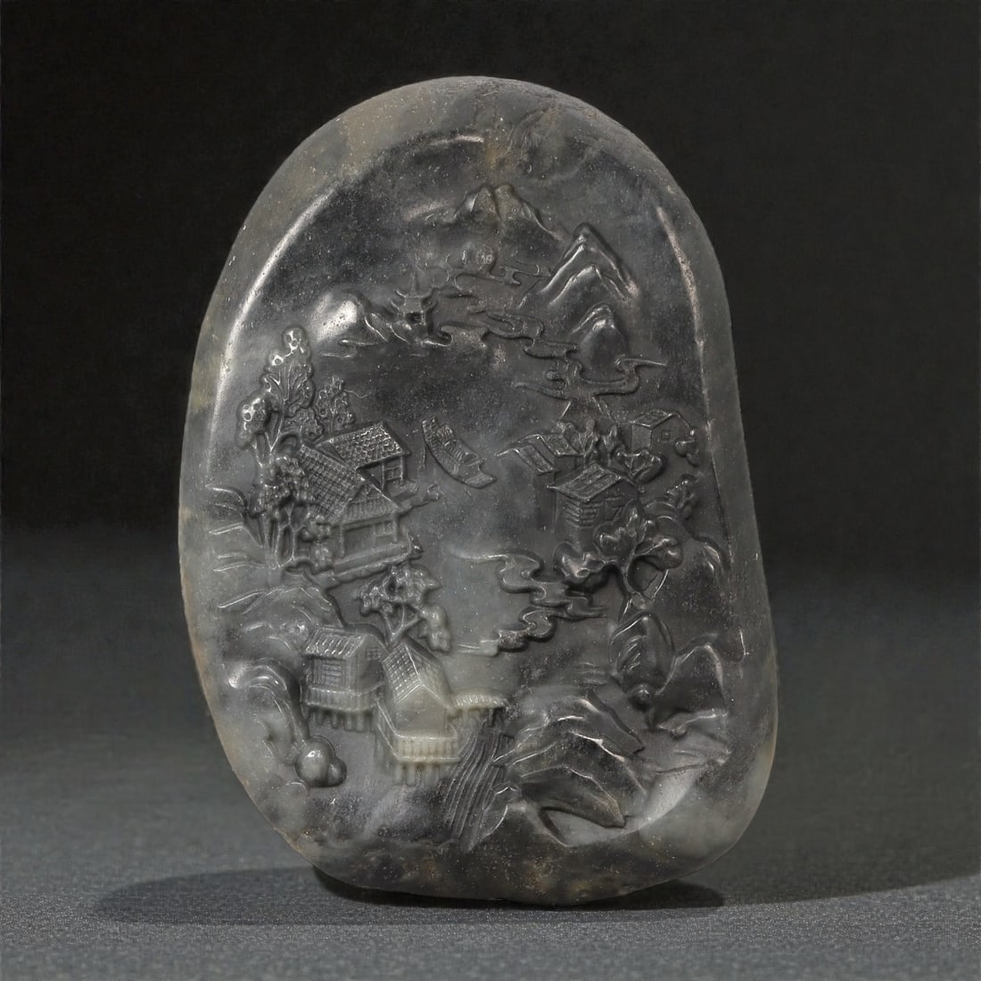 A Chinese Hetian Jade Plaque Carved with a Landscape Scene, 20th Century, 21FD: Carved from dark grey to charcoal-toned Hetian jade with subtle lighter inclusions and natural mottling, the plaque is worked in low to medium relief with a continuous landscape composition. The scene