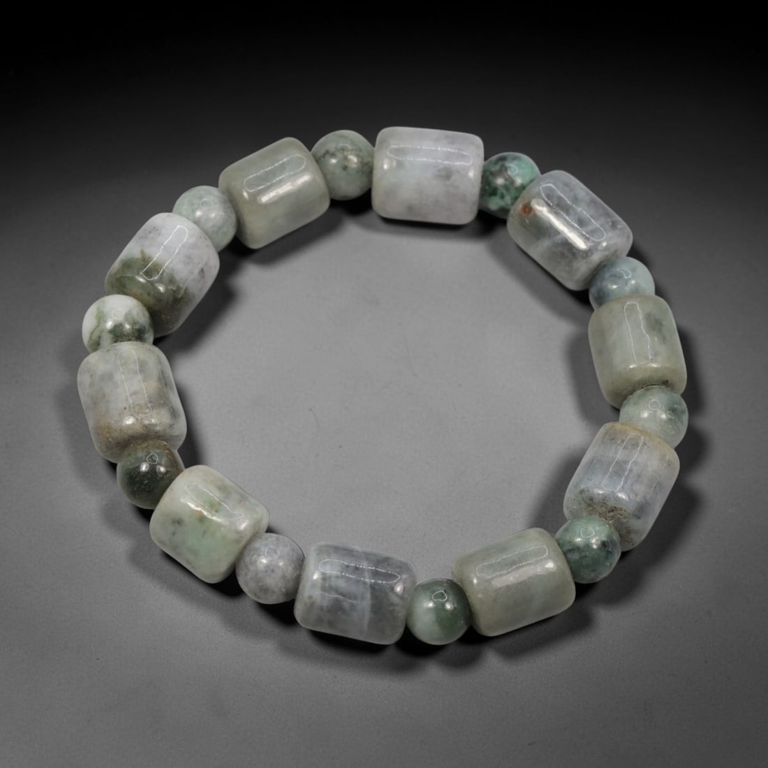 A Chinese Jadeite Jade Bead Bracelet, 20th Century, 30ZK: Composed of a single strand of barrel-shaped and spherical jadeite jade beads forming a circular bracelet. The barrel-shaped beads display natural tonal variation from pale green to deep green, with v