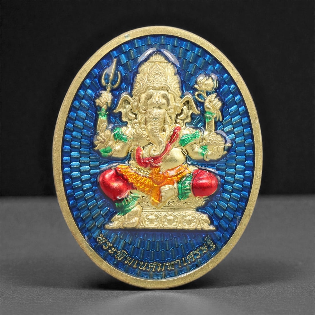 A Thai Gilt-Metal Ganesha Devotional Medallion, 21st Century, 7FR: Cast from metal with a gilt surface finish, the medallion is oval and double-sided with a raised gilt border. The obverse features a three-dimensional gilt figure of Ganesha set against a textured blu