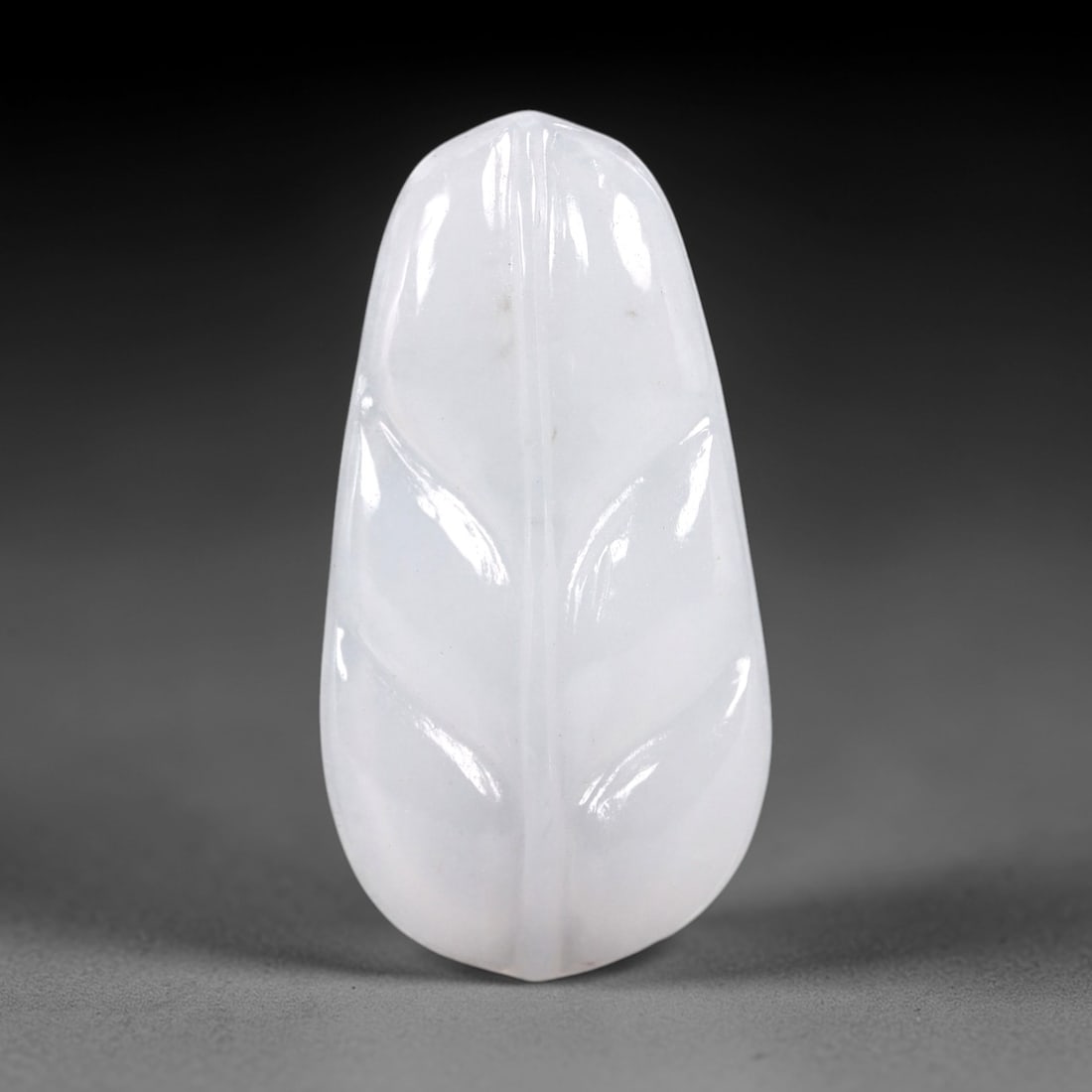 A Chinese Icy Jadeite Jade Leaf Pendant, 20th Century, 50AB: Carved from translucent icy jadeite with a pale milky-white hue and minor natural inclusions, the pendant is shaped as a stylized leaf with a rounded upper edge and a tapered lower tip. Incised lines
