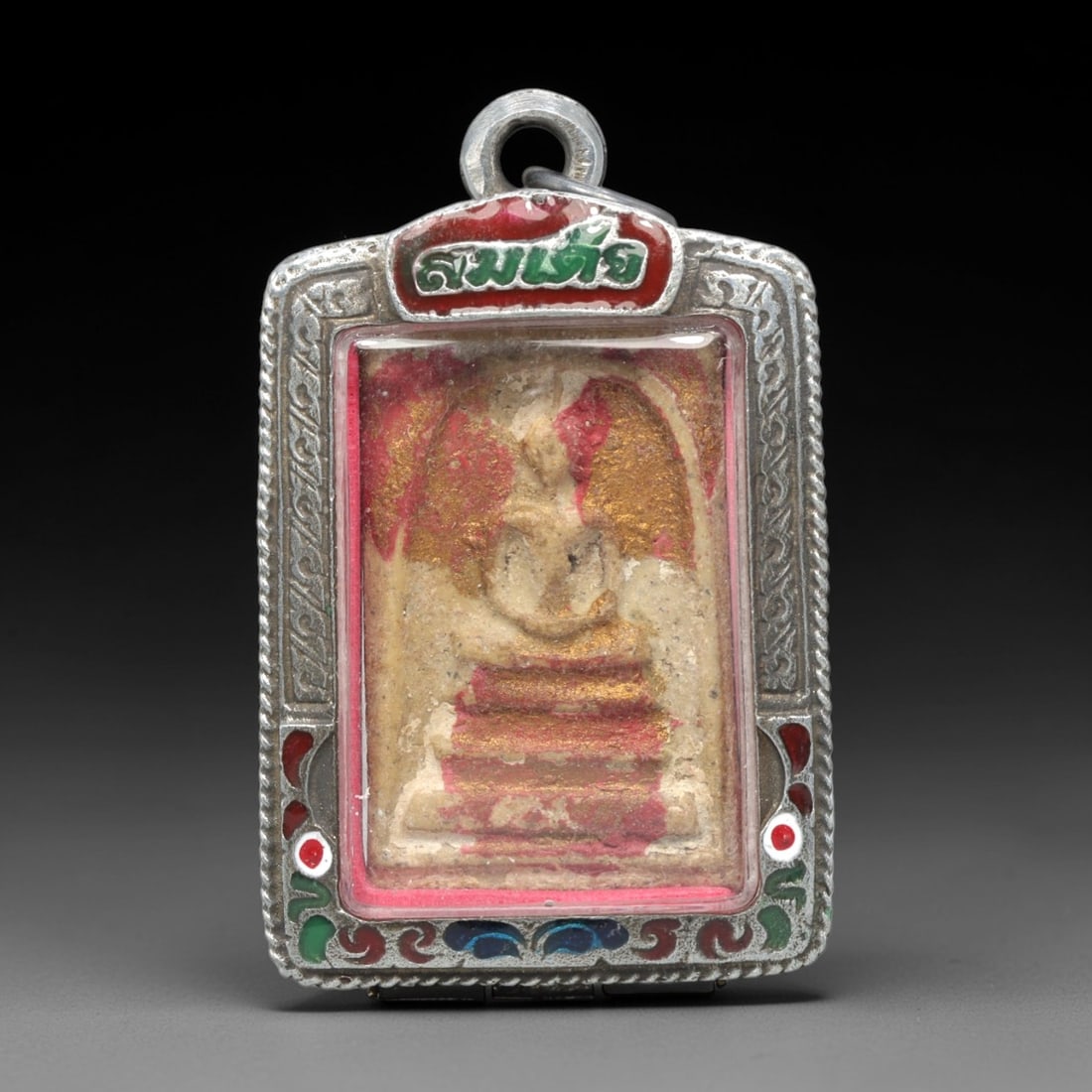 A Thai Phra Somdet Clay Amulet in a Polychrome Enamel Silver-Tone Case, 20th Century, 15ZK: This rectangular Phra Somdet amulet is crafted from sacred beige clay and encased in an ornate silver-tone metal case with a suspension loop at the apex. The obverse of the case is elaborately decorat