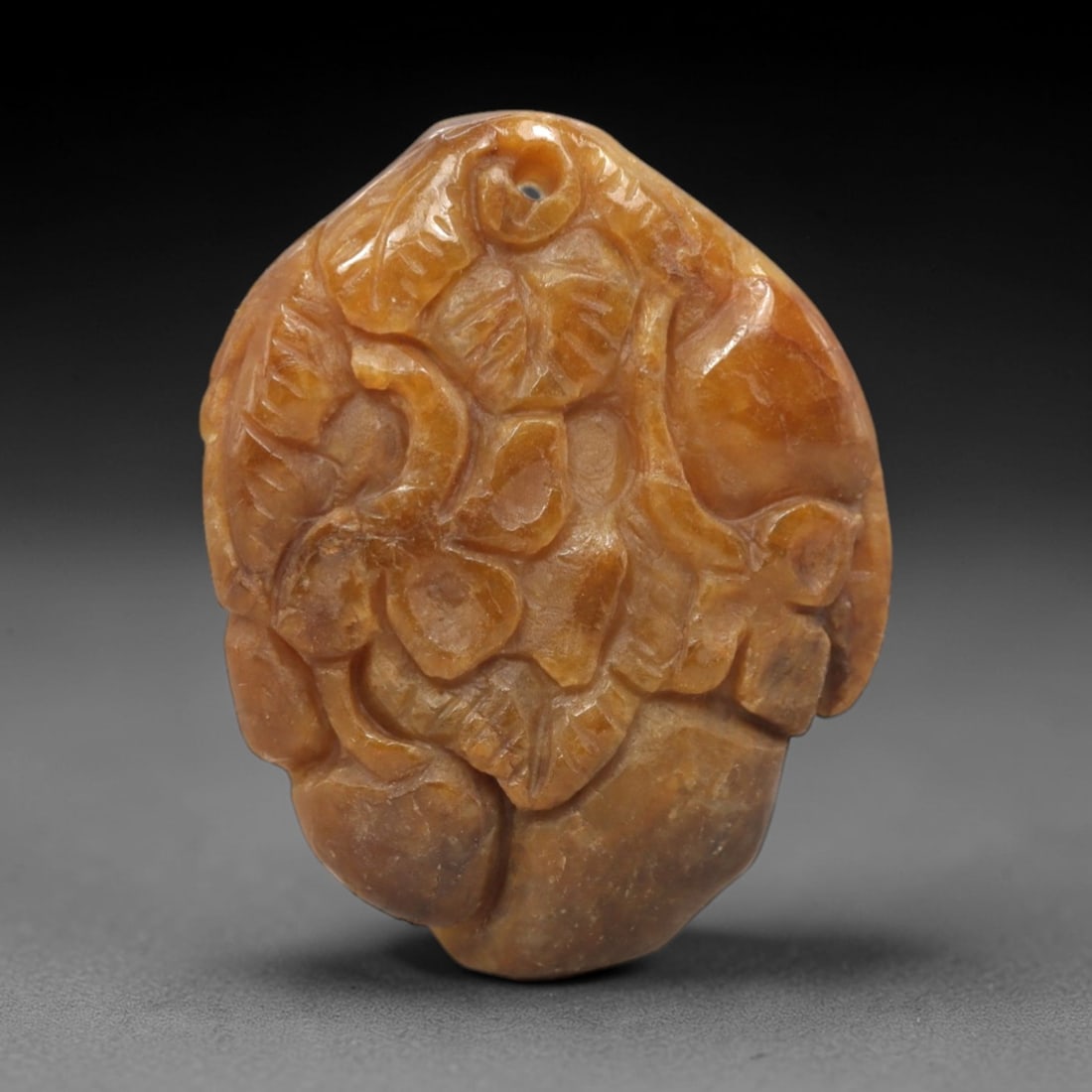 A Chinese Jadeite Jade Fruit and Floral Pendant Plaque, 20th Century, 67FR: Carved from uniform honey-yellow jadeite jade with subtle internal veining, the pendant is formed as an irregularly shaped, flattened plaque. The surface is executed in high relief to depict a dense c
