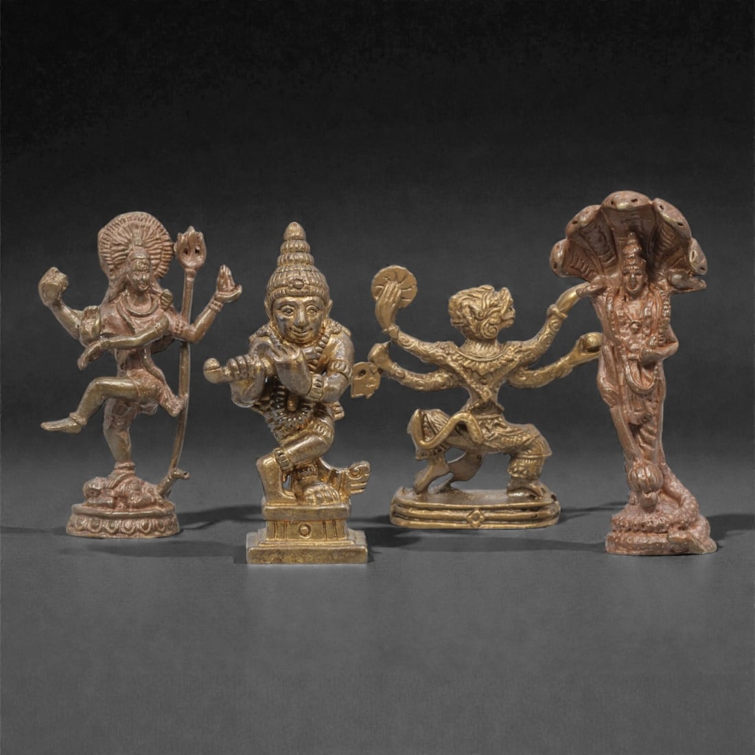 Four Thai Bronze Hindu Deity Miniature Figures, 20th Century, 13FM: Cast from bronze with a warm, aged patina, the set comprises four miniature figures representing Hindu deities: a four-armed figure in a dynamic dance pose holding a trident, a deity playing a flute,