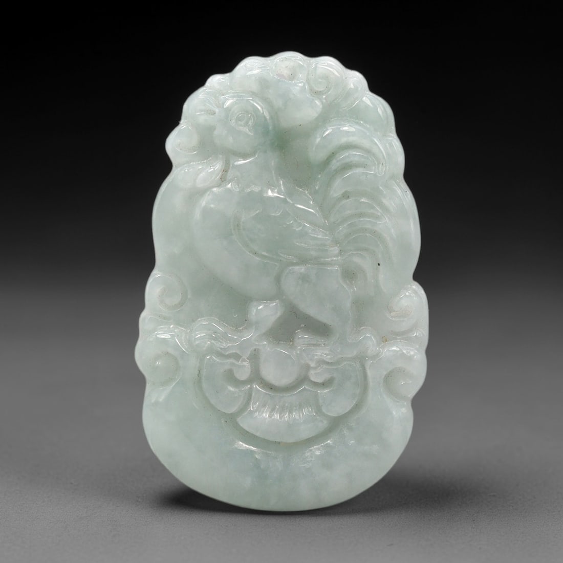 A Chinese Jade Rooster Pendant, 20th Century, 90XL: Carved from pale greenish-white jade with subtle translucency and fine natural veining, the pendant is of elongated oval form with a rounded suspension hole at the top. The surface is carved in high a