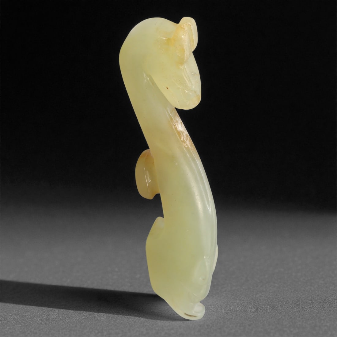 A Chinese Hetian Jade Zoomorphic Ornament, 20th Century, 80FH: Carved from pale celadon-toned Hetian jade, the ornament is rendered in a stylized zoomorphic form with an elongated, sinuous body rising in a gentle curve. The head is subtly defined with a rounded s