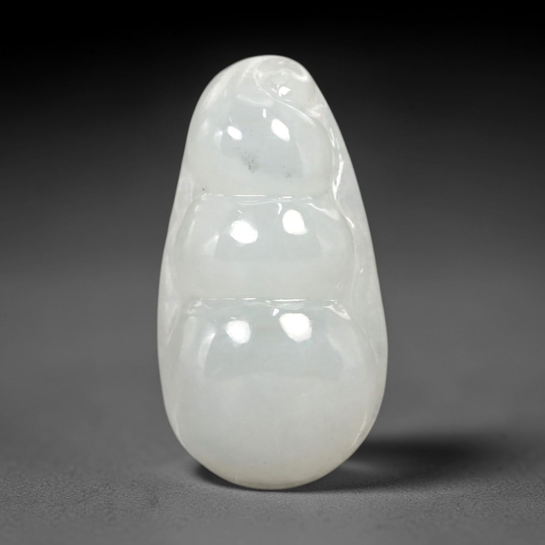 A Chinese Icy Jadeite Jade Bean Pendant, 20th Century, 57AB: Carved from translucent icy jadeite with a pale milky-white hue and minor natural inclusions, the pendant is shaped as a stylized three-segmented bean pod. Smooth, rounded contours define each segment