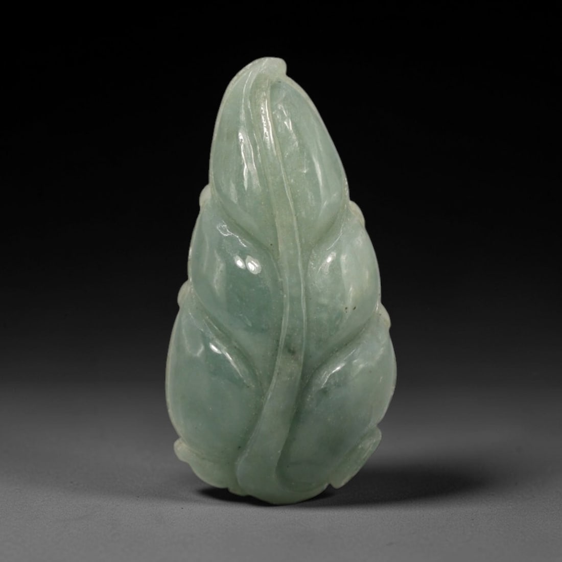 A Chinese Jadeite Jade Leaf-Form Pendant, 20th Century, 49FR: Carved from uniform celadon jadeite jade with a smooth, glossy finish and subtle internal veining, the pendant is formed as a stylized leaf. The surface is executed in low relief, with incised lines d