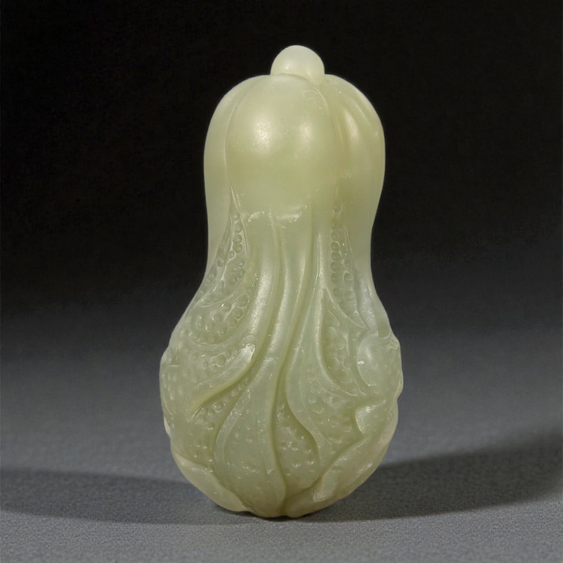 A Chinese Nephrite Jade Cabbage Carving, 20th Century, 38FA: Carved from pale celadon nephrite jade with a high degree of translucency and subtle tonal variation, the object is modeled in the form of a cabbage head rendered in the round. The upper section is sm