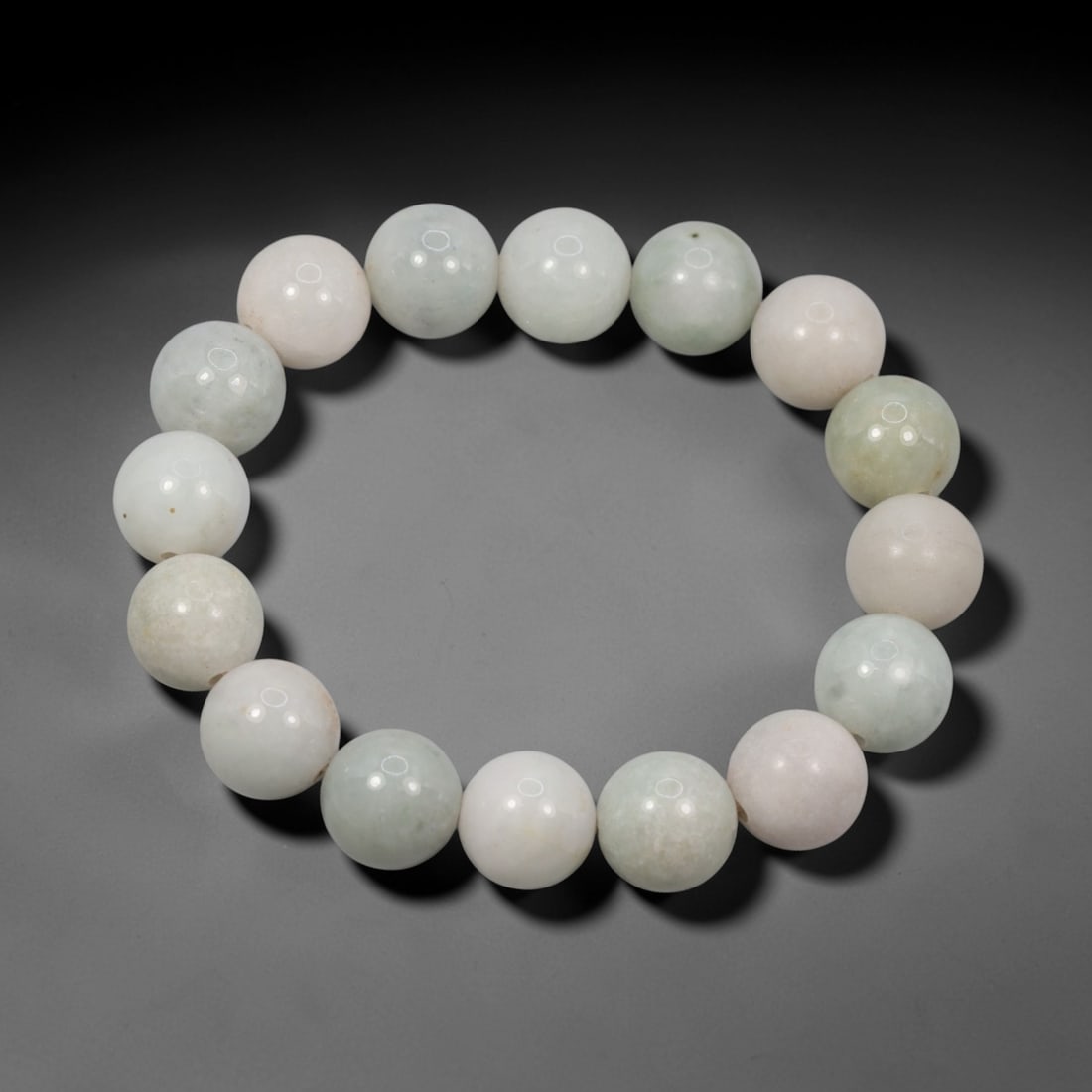 A Chinese Jadeite Jade Bead Bracelet, 20th Century, 41ZK: Composed of a single strand of spherical jadeite jade beads forming a circular bracelet. The beads exhibit a distinctive bi-colour palette of pale celadon green and soft blush pink, with natural inter