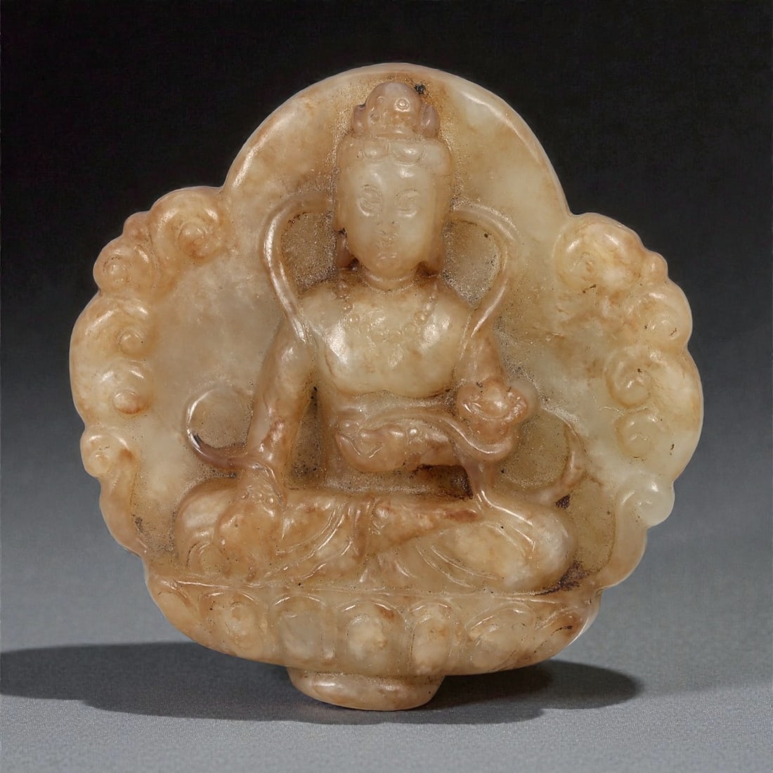 A Chinese Jade Plaque Carved with a Seated Bodhisattva, 19th-20th Century, 27FD: Carved from translucent jade of pale honey-brown tone with areas of natural clouding and darker inclusions, the plaque is worked in relief with a seated bodhisattva shown frontally. The figure is depi