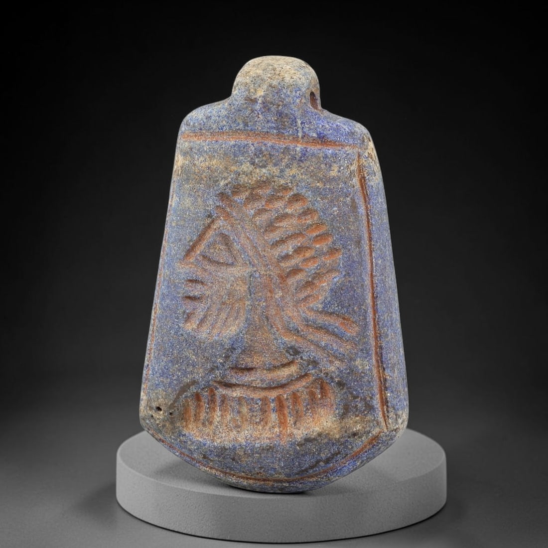 Ancient Lapis Lazuli Amulet - Near Eastern Symbolic Figurine, 6BA: Carved from lapis lazuli, the amulet takes a trapezoidal form with a suspension loop at the top, designed for wear as a protective talisman. The front face is incised with a stylized symbolic motif, r