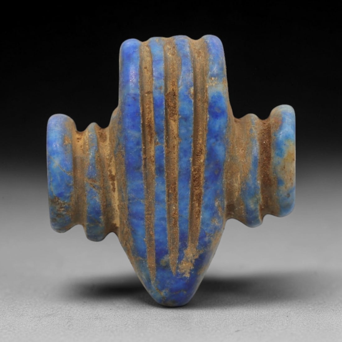 Ancient Lapis Lazuli Amulet - Egyptian Ritual Pendant, 31ZT: Carved from lapis lazuli, this amulet features a symmetrical form with a pointed lower end, flanked by two rounded side lugs, and a ridged upper section pierced for suspension. Its surface is incised