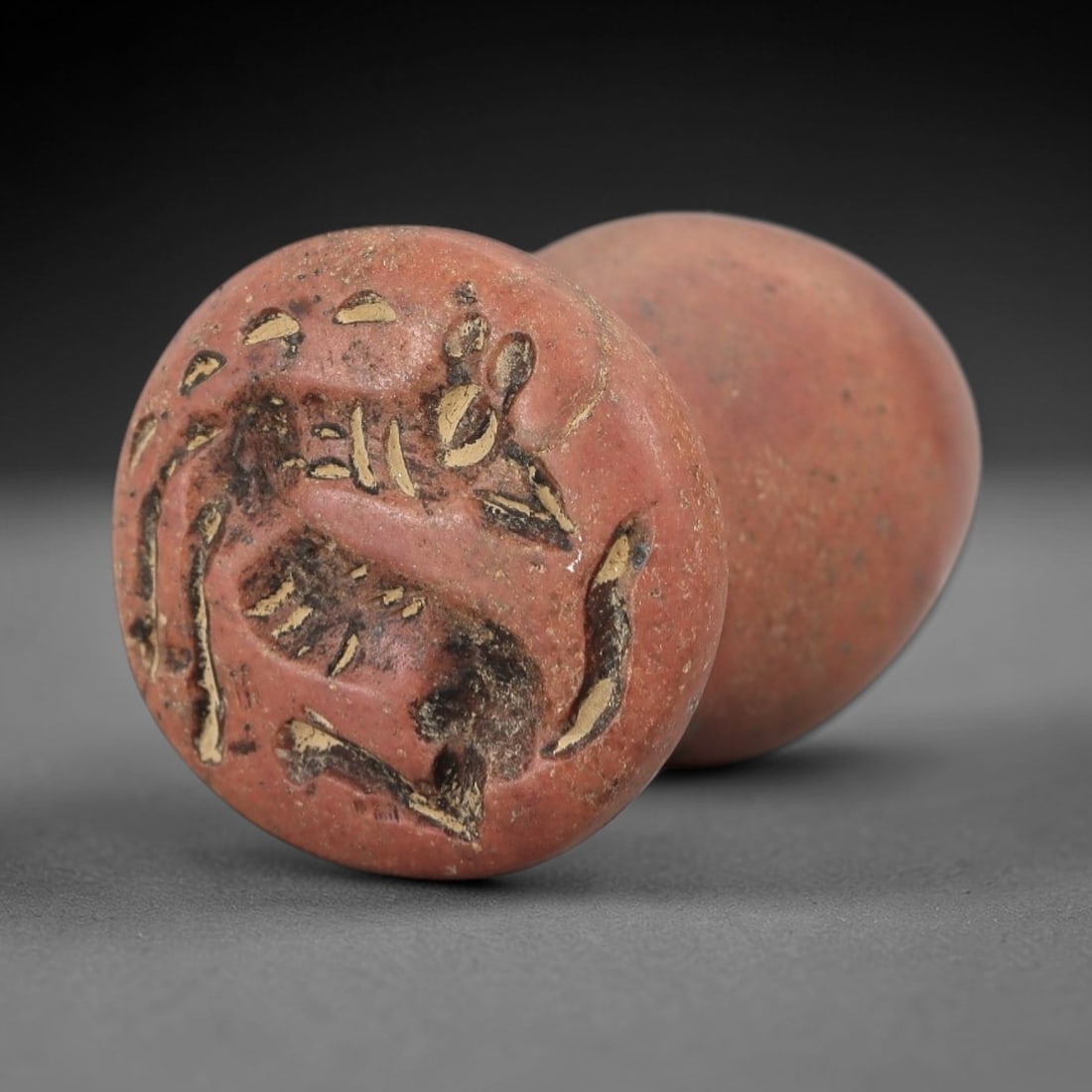 Ancient Stone Stamp Seal - Near Eastern Reclining Beast Impression, 1AM: This mushroom-shaped stamp seal is carved from a dense, reddish-brown stone with a matte, earthy patina and contrasting lighter mineral inclusions. The flat circular face bears a deep intaglio impress