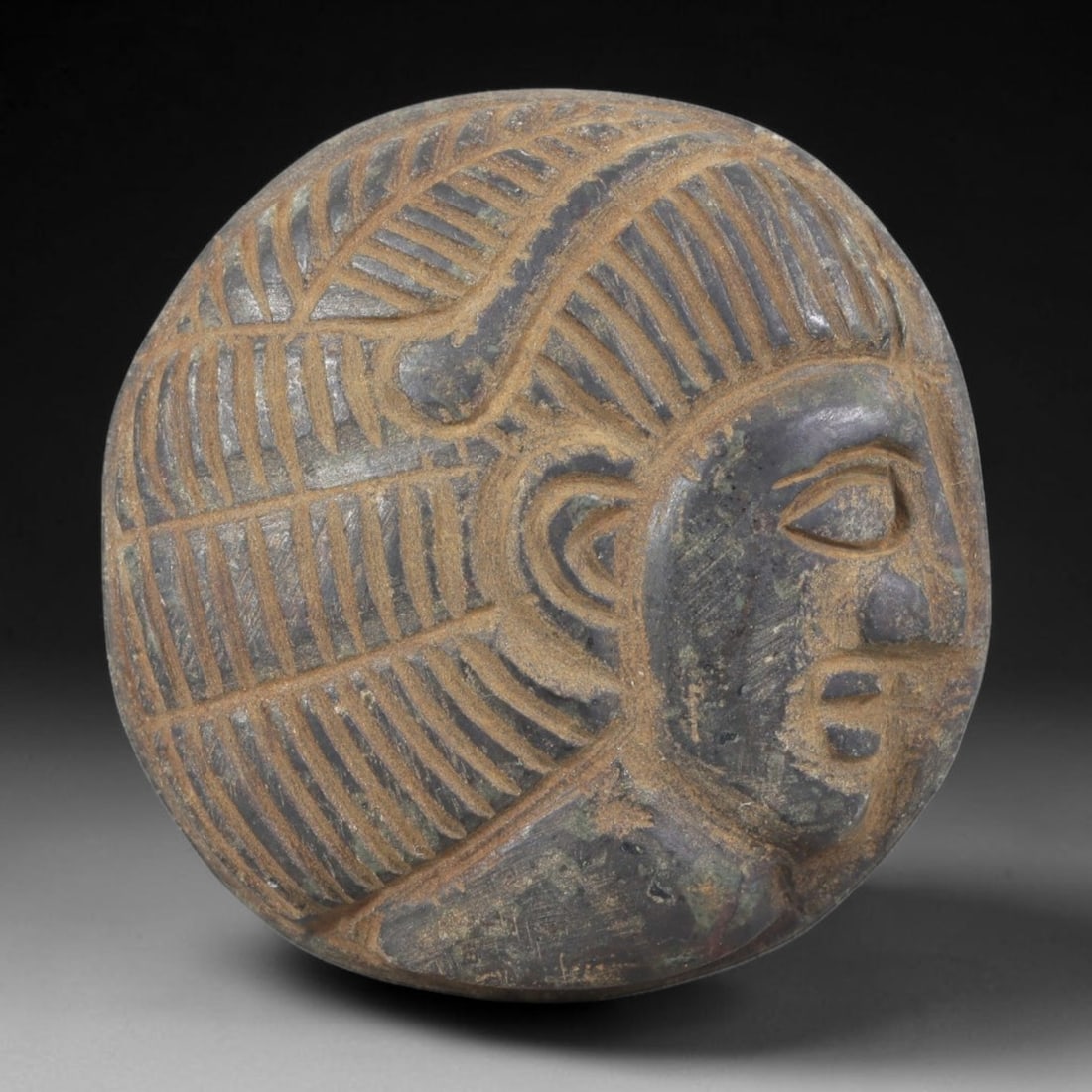 Ancient Stone Amulet - Near Eastern Bust Plaque Pendant, 39FY: Carved from dark stone, the amulet is a circular plaque crafted in the ancient Near Eastern style, featuring a raised relief portrait of a human bust in profile. The surface bears incised details rend