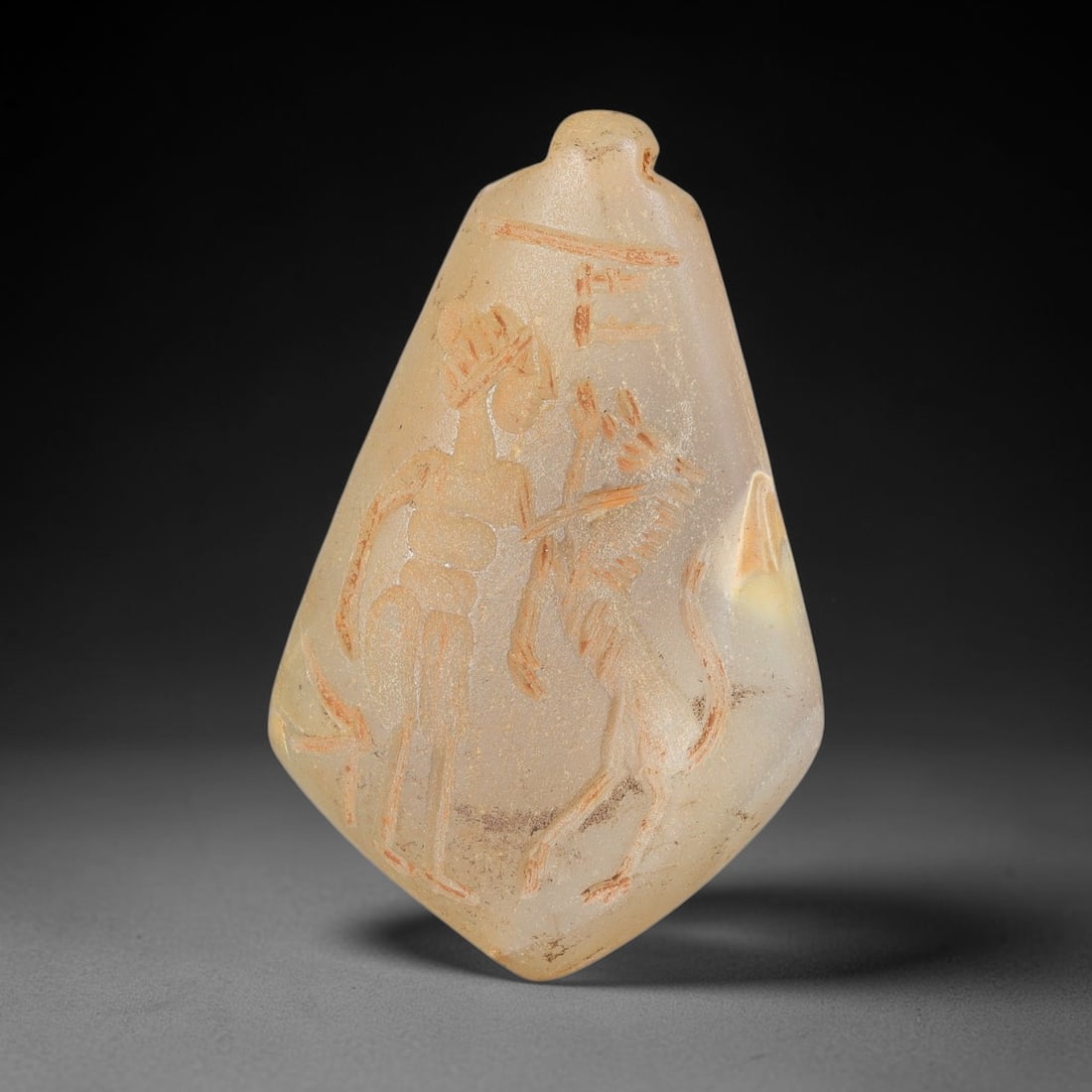 Ancient Chalcedony Hunter & Beast Amulet - Near Eastern Carved Pendant, 24BA: Carved from chalcedony, the amulet takes the form of a flattened teardrop-shaped pendant with a drilled suspension lug at the top for wear. The surface features a relief-carved figural scene, rendered