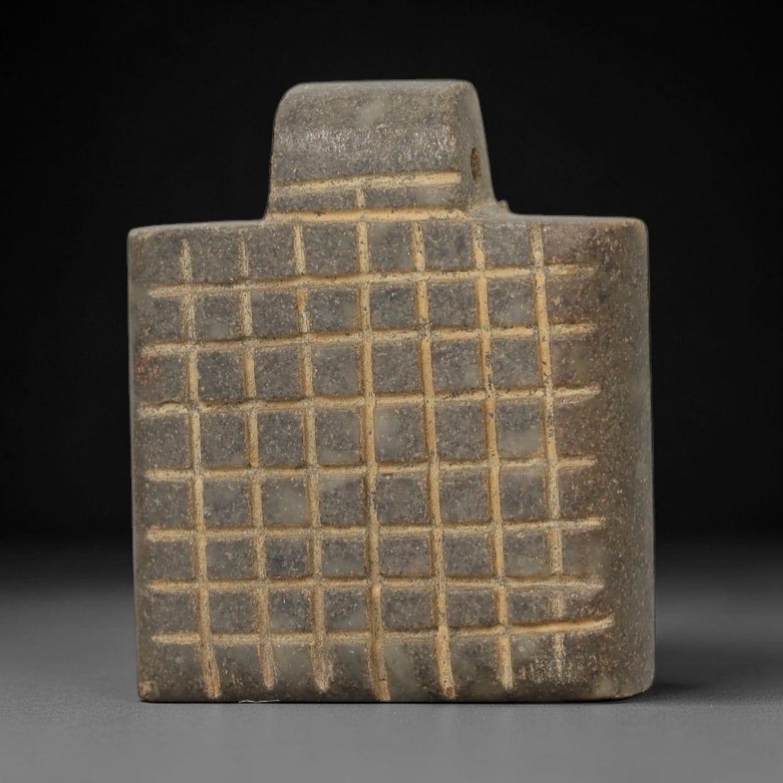 Ancient Stone Grid Amulet - Near Eastern Pendant, 44AE: This artifact is a carved stone amulet of Near Eastern origin, crafted from a mottled grey-green stone with lighter mineral inclusions and a matte, aged patina. Its form consists of a thick, square-sh